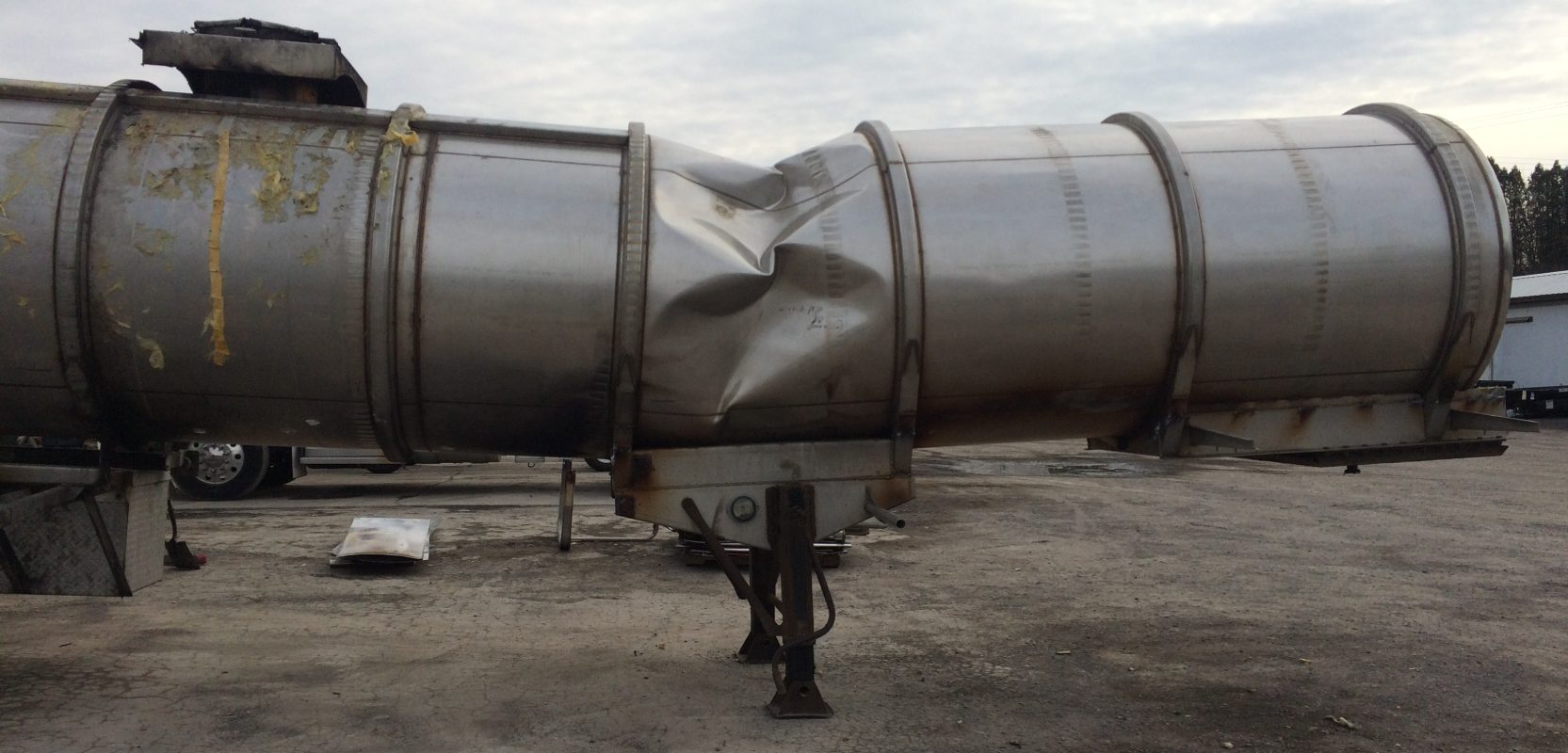 Damaged stainless milk tanker trailer before repair